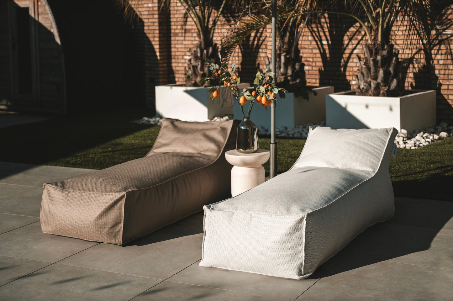 Two lounge chairs on a patio with a garden and building in the background