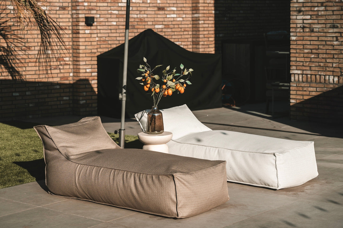 Outdoor seating area with beige and white bean bags and a small table with flowers against a brick wall.